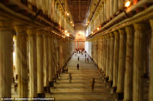Large pillars are lined up on either side of of a wide walkway with a few people scattered along.